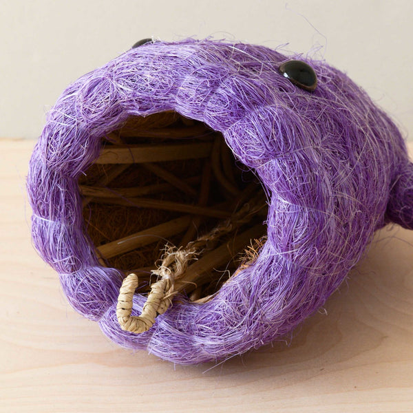 Purple woven cat bed with a textured surface on a light wooden floor.