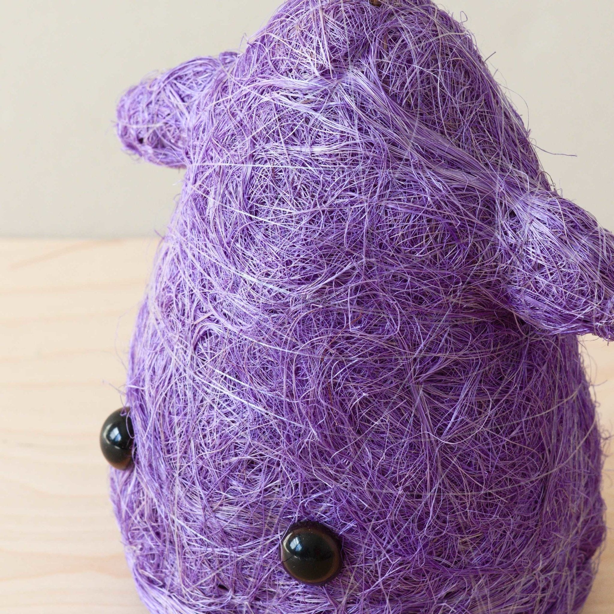 Purple yarn ball with black buttons on a wooden surface
