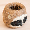 Heart-shaped decorative item made of twine with a raccoon face design on a beige background