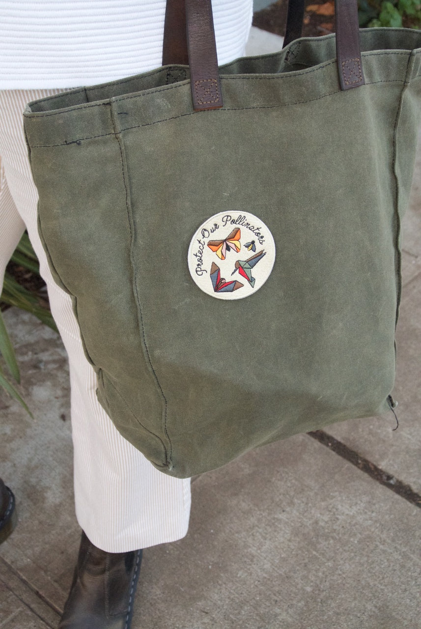 Pollinator Pride patch and sticker kit styled on everyday gear like a jacket and notebook