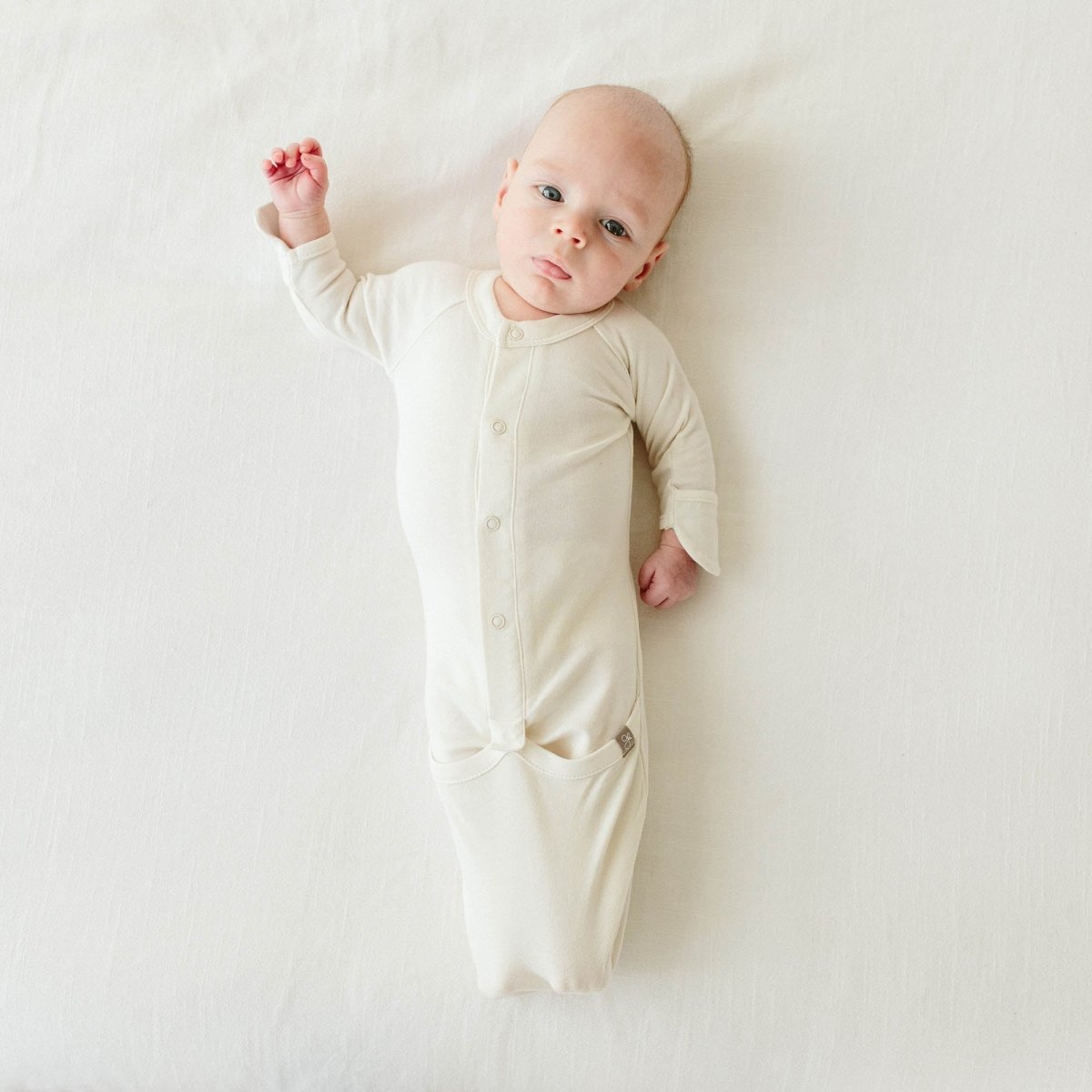 Baby wearing a cream-colored onesie lying on a white surface