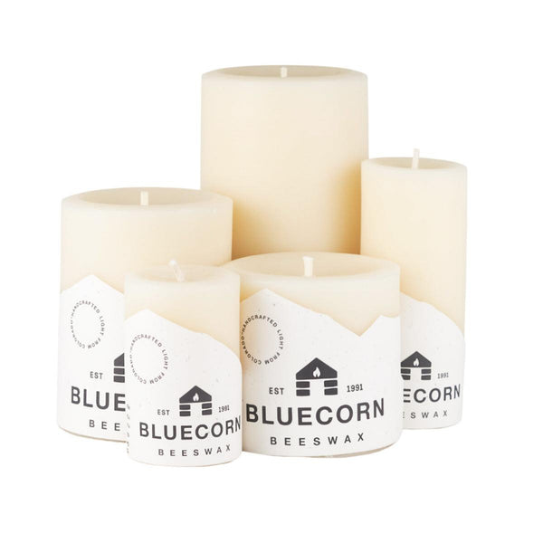 Set of four white candles with Bluecorn Beeswax labels on a white background