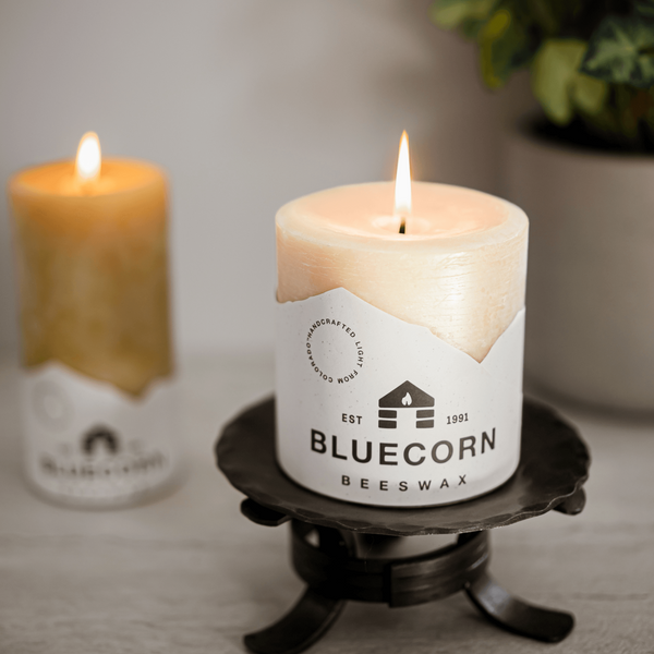 Candle with Bluecorn Beeswax label on a stand, with another candle in the background.