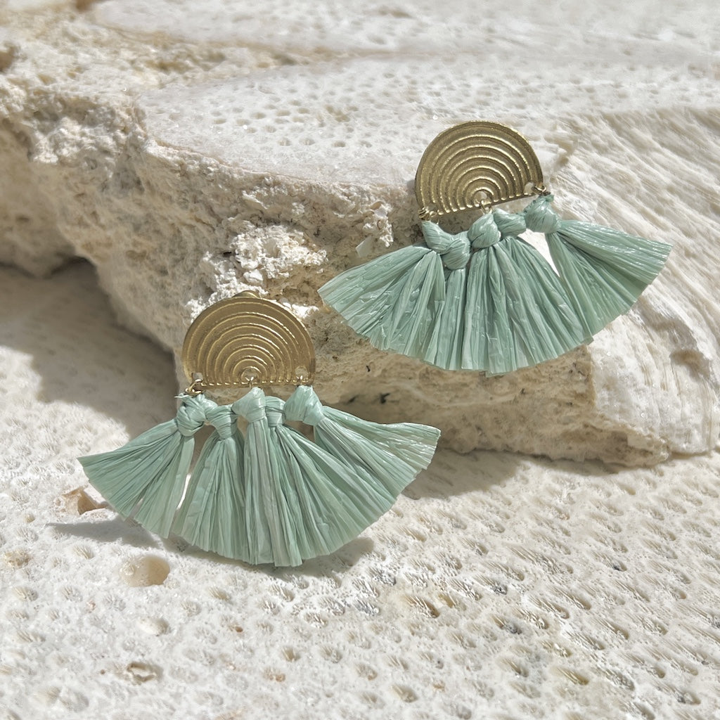 Pair of mint green tassel earrings with gold accents on a textured stone surface.