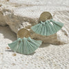 Pair of mint green tassel earrings with gold accents on a textured stone surface.