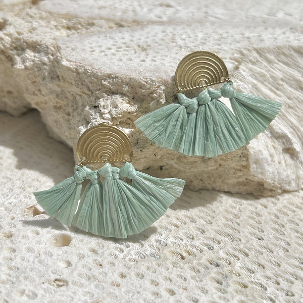 Pair of mint green tassel earrings with gold accents on a textured stone surface.