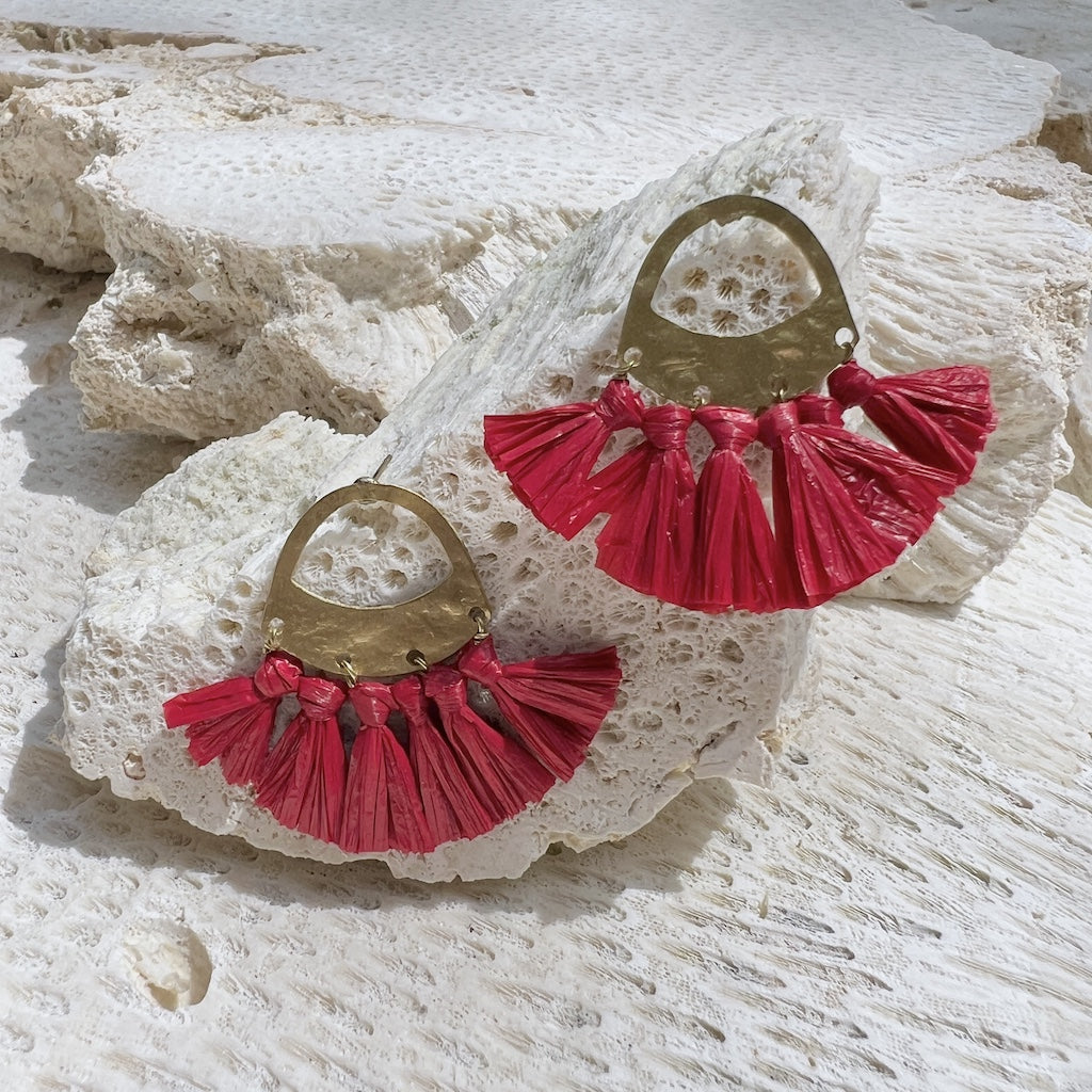 Red tassel earrings on a textured white stone surface