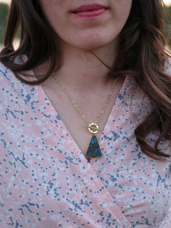 Close-up of a raw-cut labradorite triangle pendant on a brass chain by Fair Anita