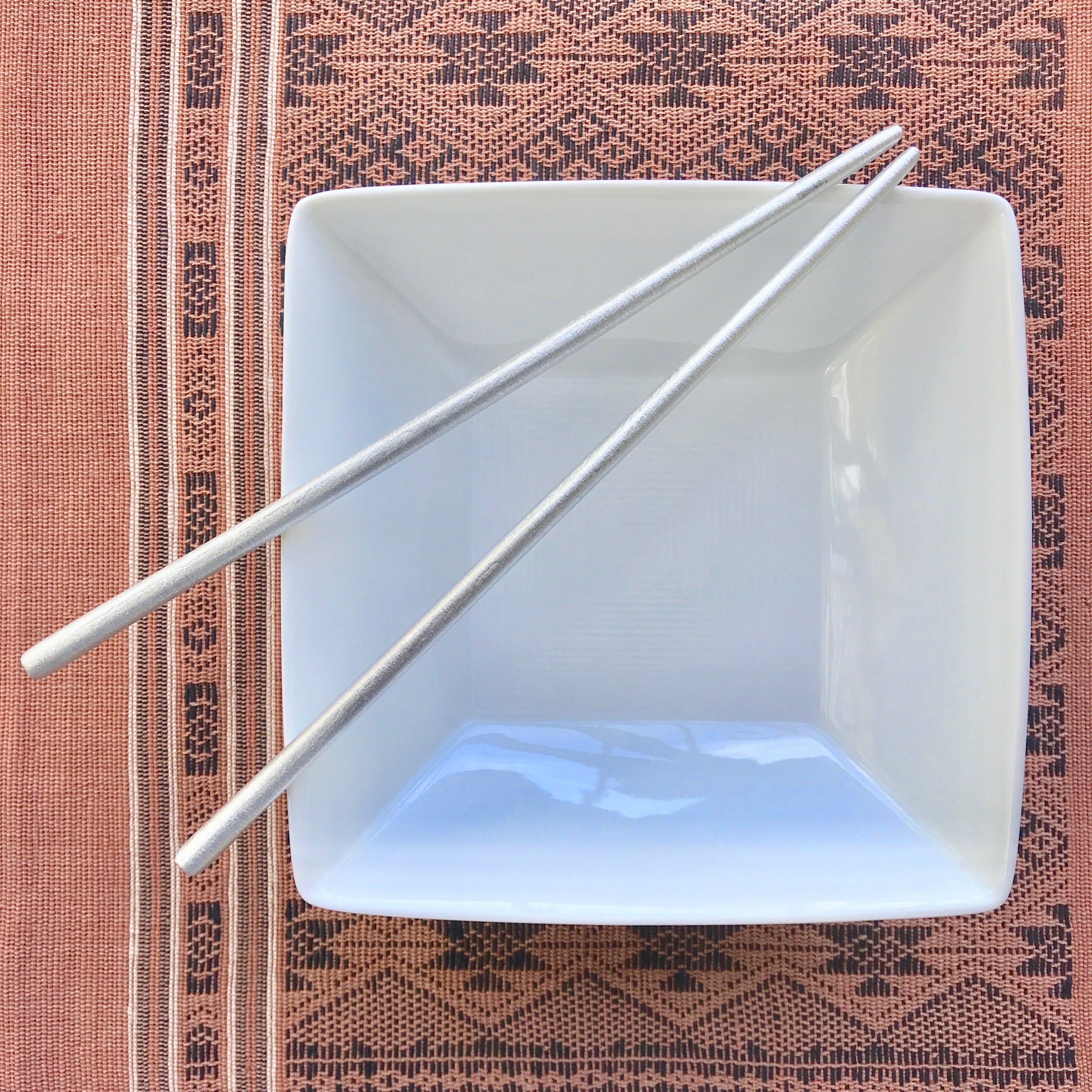 White square bowl with chopsticks on a patterned fabric background