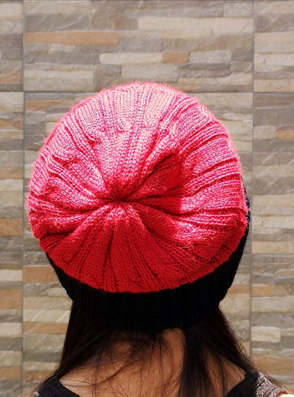 Red knitted beanie worn by a person against a stone wall background