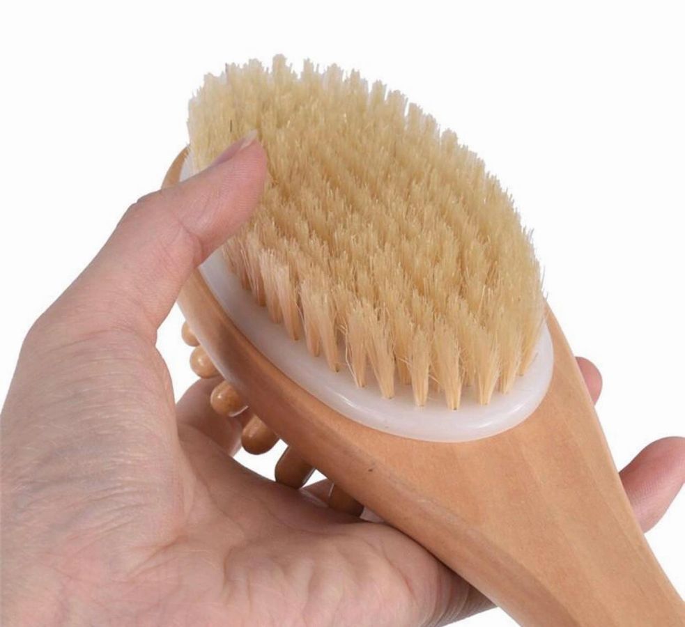 Hand holding a wooden brush with bristles against a white background