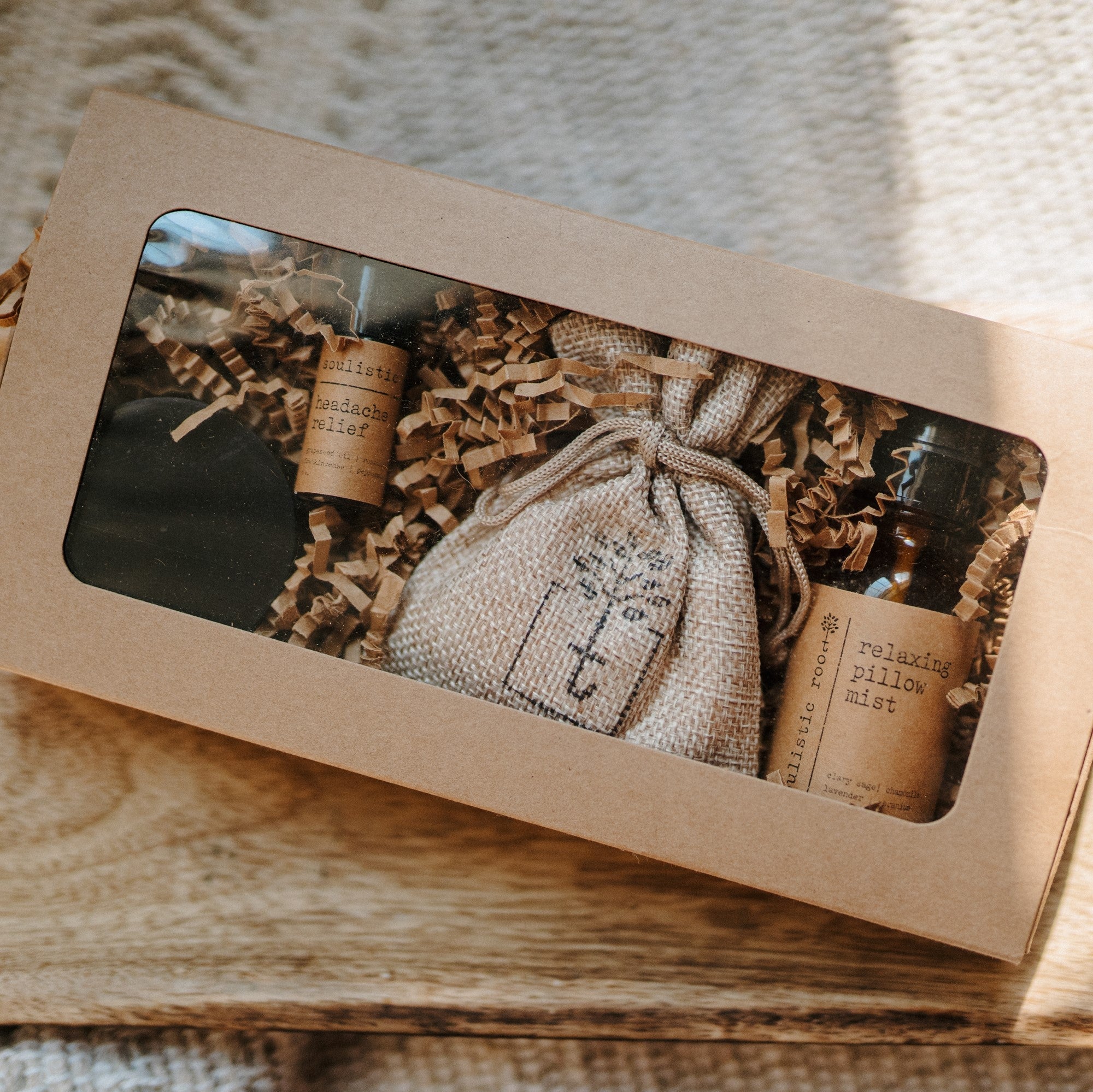 Gift set with a bottle, pouch, and candles in a brown box on a wooden surface.