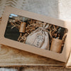 Gift set with a bottle, pouch, and candles in a brown box on a wooden surface.