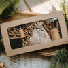 Gift set with bottles and a pouch in a brown box, surrounded by greenery.
