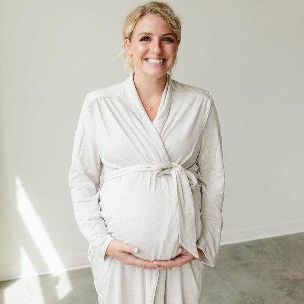 Pregnant woman wearing a white robe against a plain background