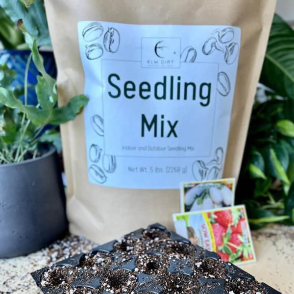 Bag of seedling mix with a label, surrounded by plants and seed packets.