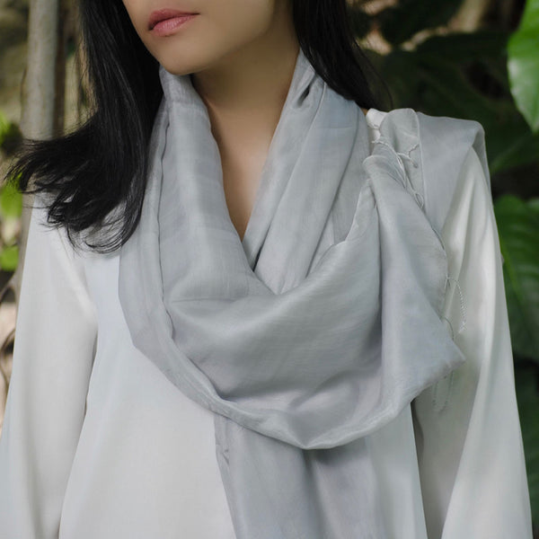 Person wearing a light gray scarf with a blurred natural background