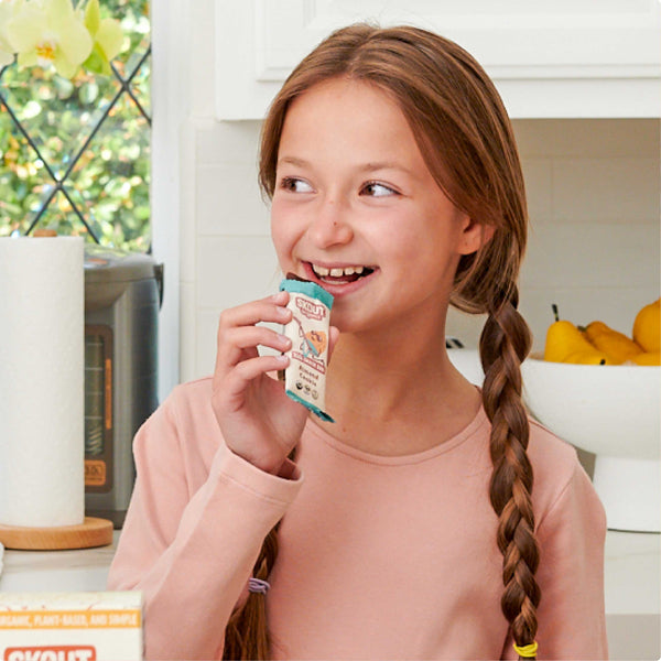 Young girl holding a snack package in a kitchen setting