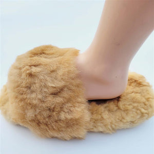 Person wearing brown fluffy alpaca fur slide-in slippers on a light gray background