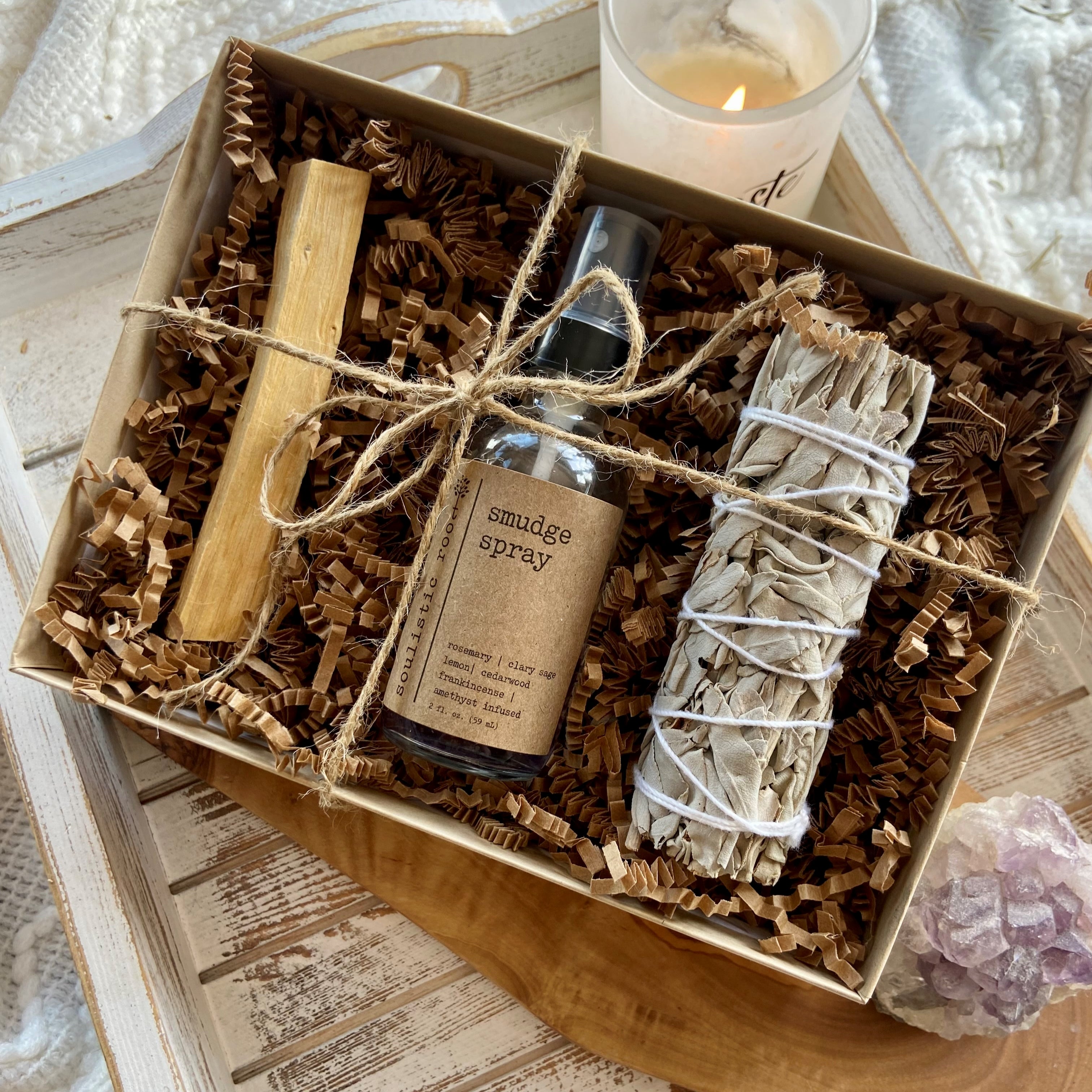 Gift set with smudge spray, wooden stick, and sage in a box on a textured surface.