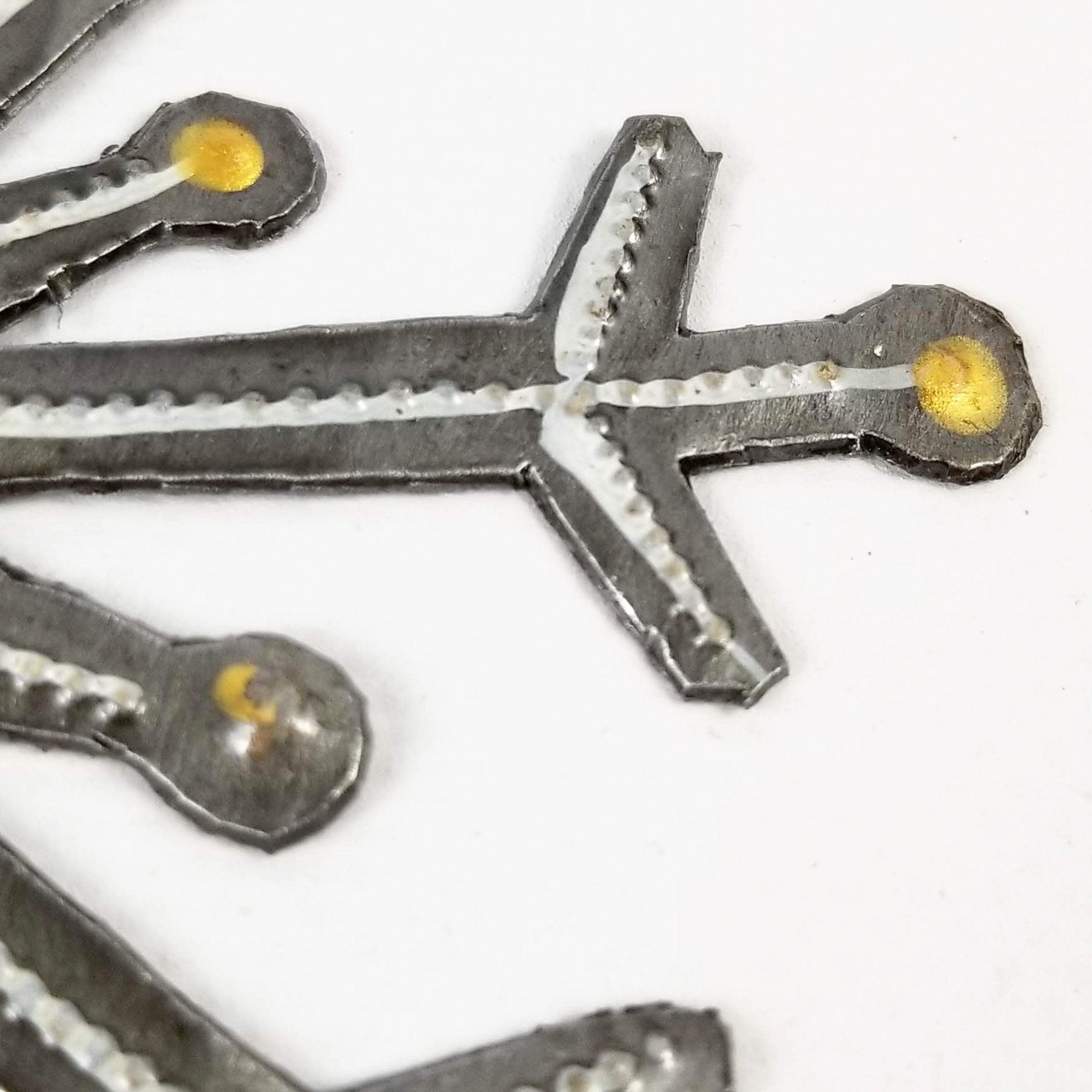 Metallic cross-shaped object with yellow accents on a white background