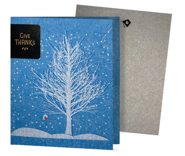 A blue folding greeting card with a white tree and red bird design, and the text 'Give Thanks' on the front.