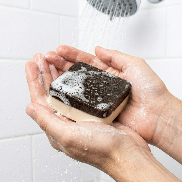 Person holding a bar of soap with water droplets in a bathroom setting
