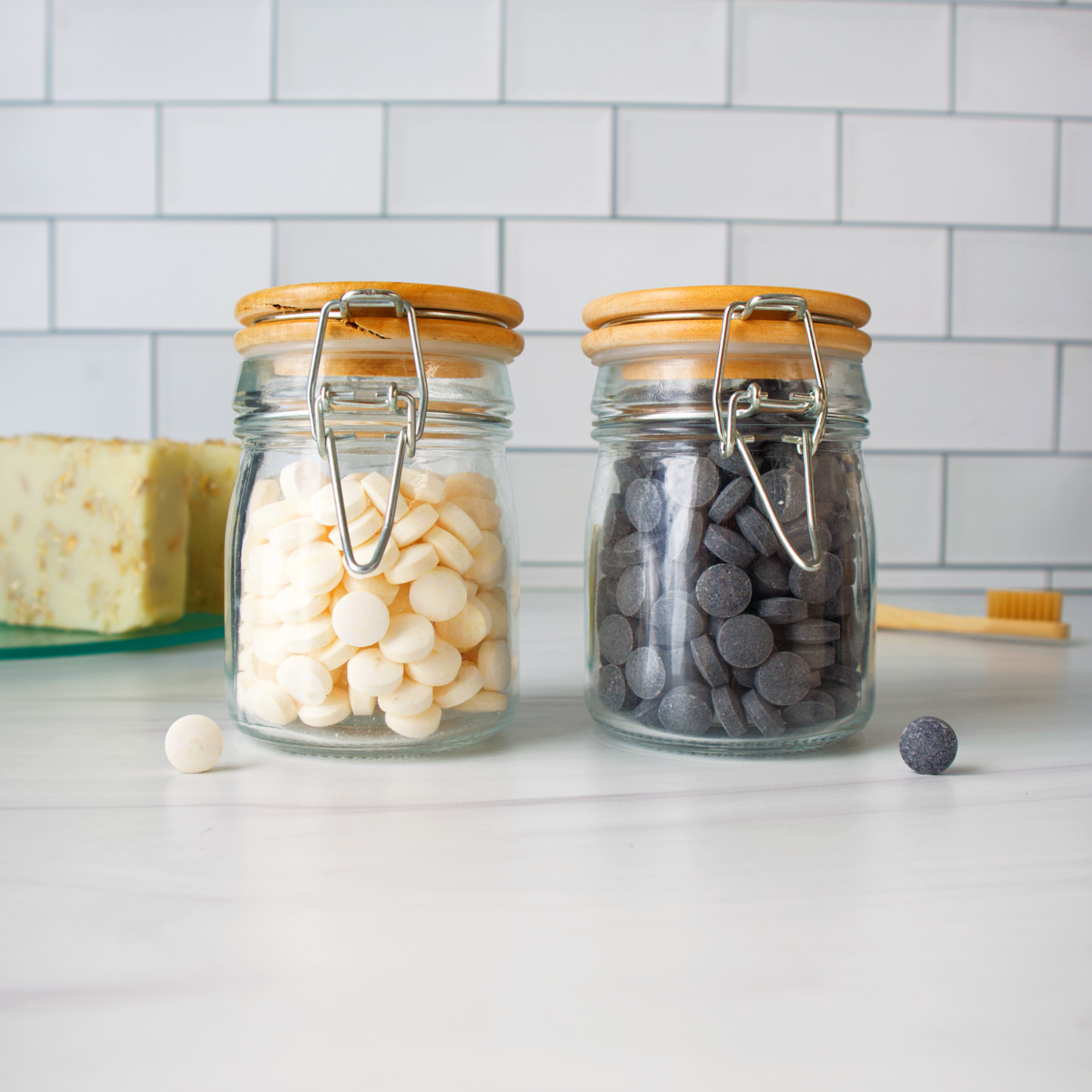 Two glass jars with wooden lids on a kitchen counter, one containing white items and the other containing gray items.