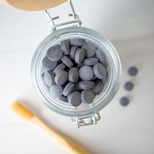 Jar of gray tablets with a wooden spoon on a light surface