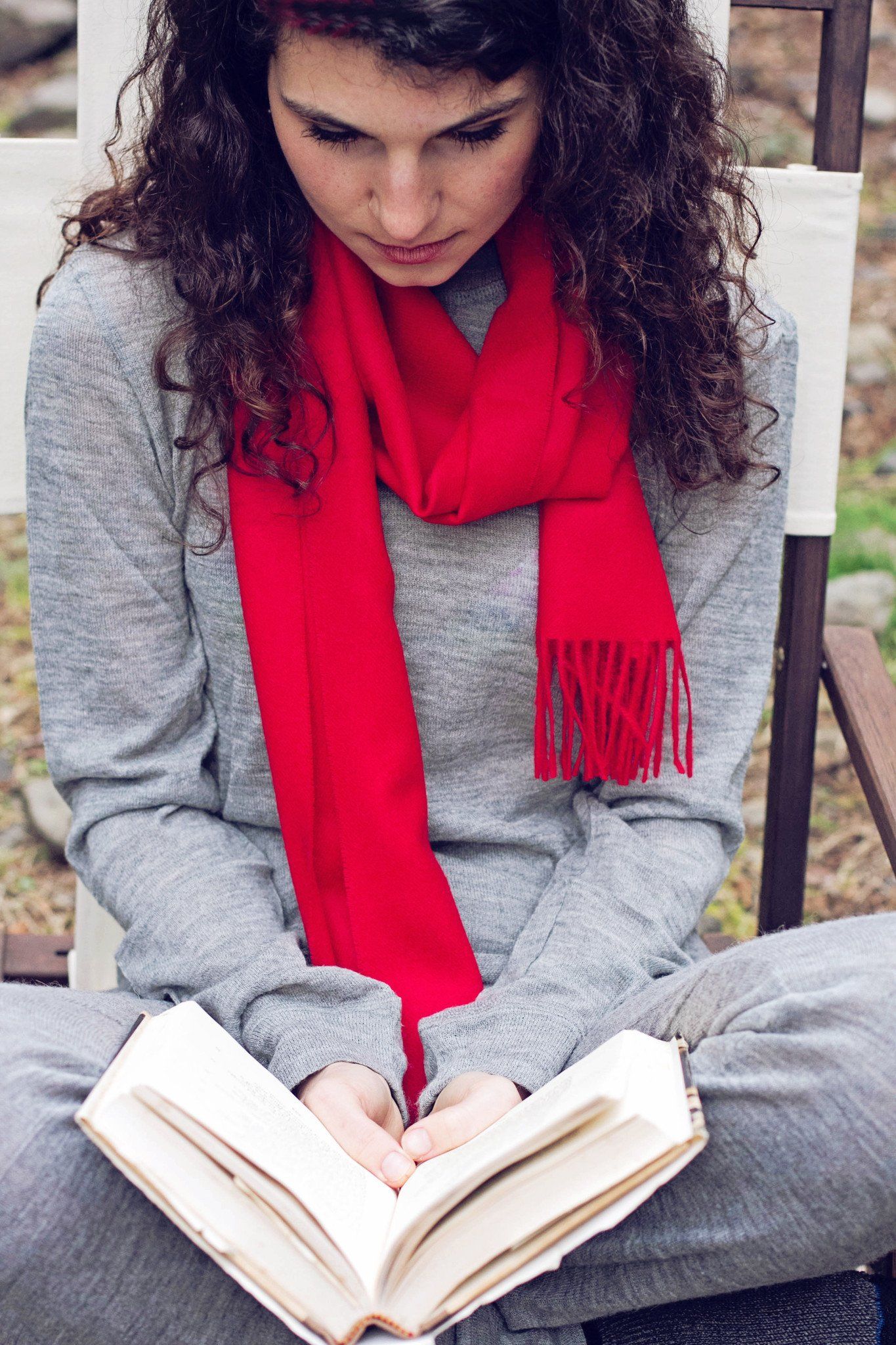 Woman wearing a red scarf and reading a book outdoors