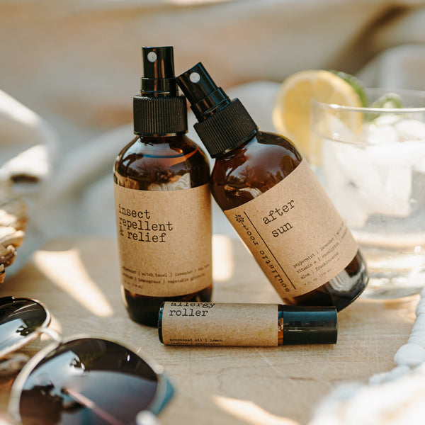 Three bottles of natural skincare products on a wooden surface with sunglasses and a glass in the background.