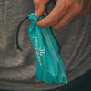 Hand holding a teal drawstring bag with 'joycoast' branding against a blurred background.