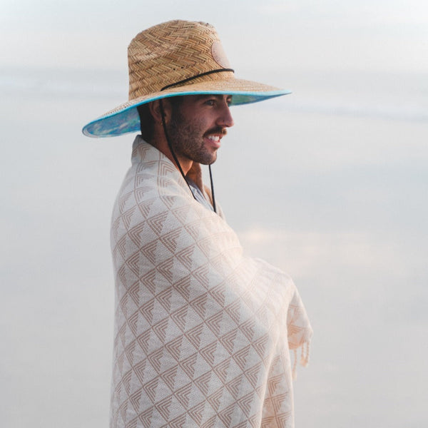 Man wearing a straw hat and patterned towel against a light background