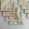 Close-up of Dot and Army sweary bad word cocktail coasters showing colorful edging and bold letter design on linen blend fabric