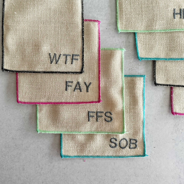 Close-up of Dot and Army sweary bad word cocktail coasters showing colorful edging and bold letter design on linen blend fabric