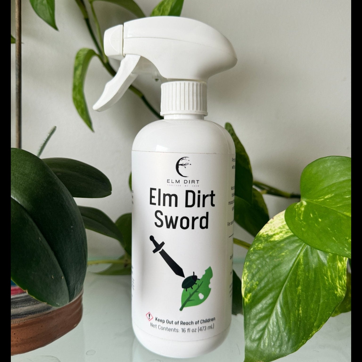 White spray bottle labeled 'Elm Dirt Sword' with green leaves in the background