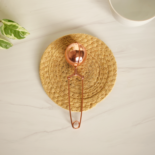 Rose gold tea strainer on a woven mat with a light background