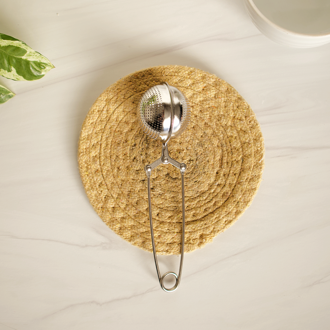 Metallic tea infuser on a woven coaster with a light background