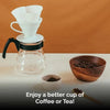 Coffee brewing setup with a glass carafe, coffee filter, and wooden bowl of coffee beans on a white surface.