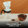 Coffee brewing setup with a glass carafe, coffee filters, and wooden bowl of coffee beans on a white surface.