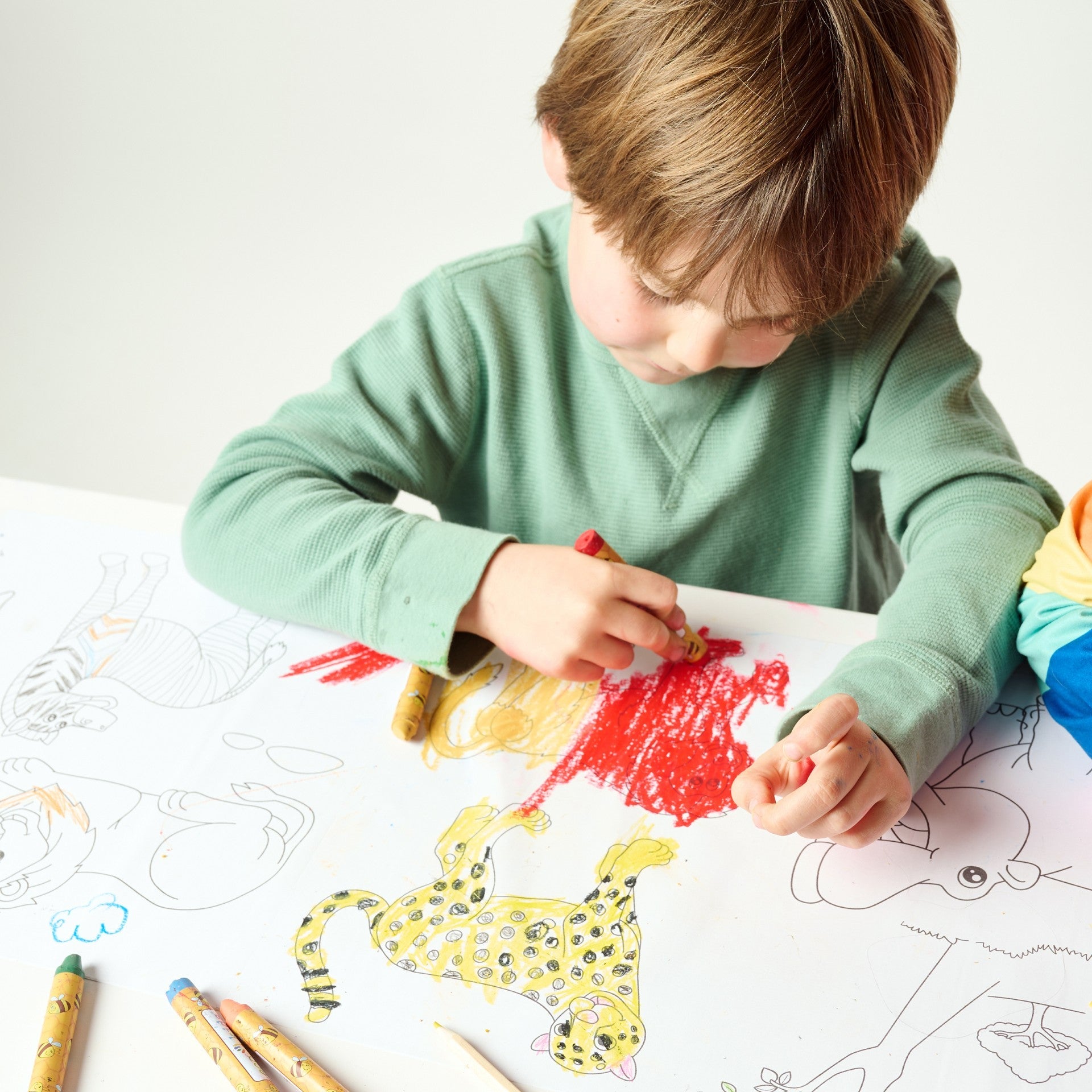 Child coloring a picture of a leopard with crayons on a white sheet of paper.