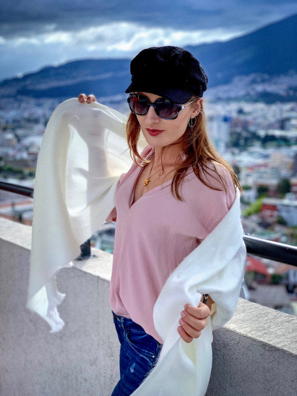 Woman in pink top and black cap with white scarf against a cityscape background