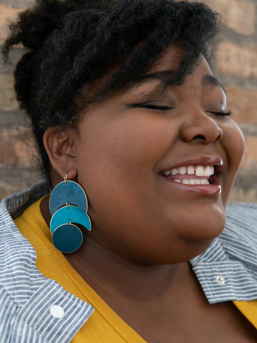 Fair Anita dark matte blue moon phase earrings styled against a neutral background