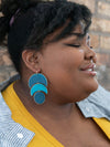 Close-up of trendy dark matte blue statement earrings by Fair Anita showing painted crescent moon detail
