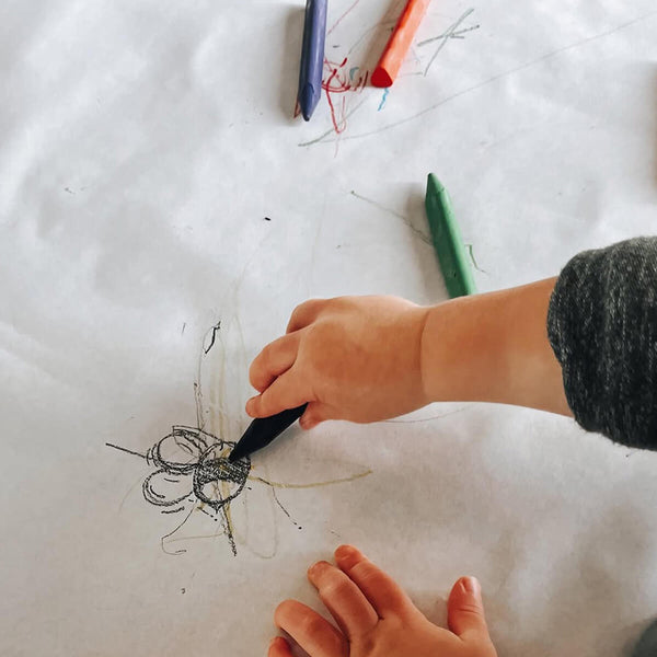 Child using triangle-shaped beeswax crayons to draw on paper