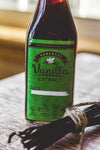Bottle of homemade vanilla extract with a green label on a wooden surface.