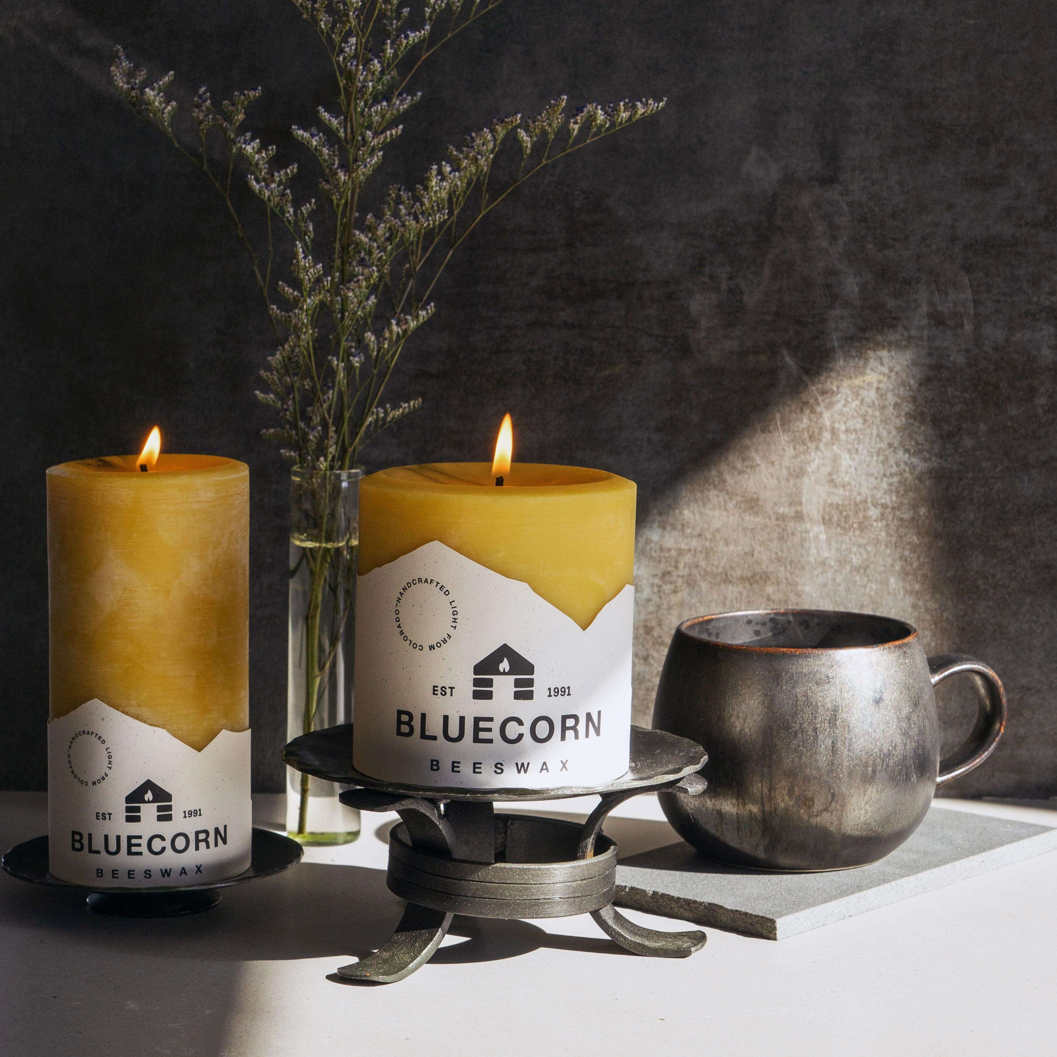 Two lit candles with 'Bluecorn' branding on a dark background