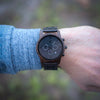 Wooden wristwatch on a person's wrist with a blurred natural background