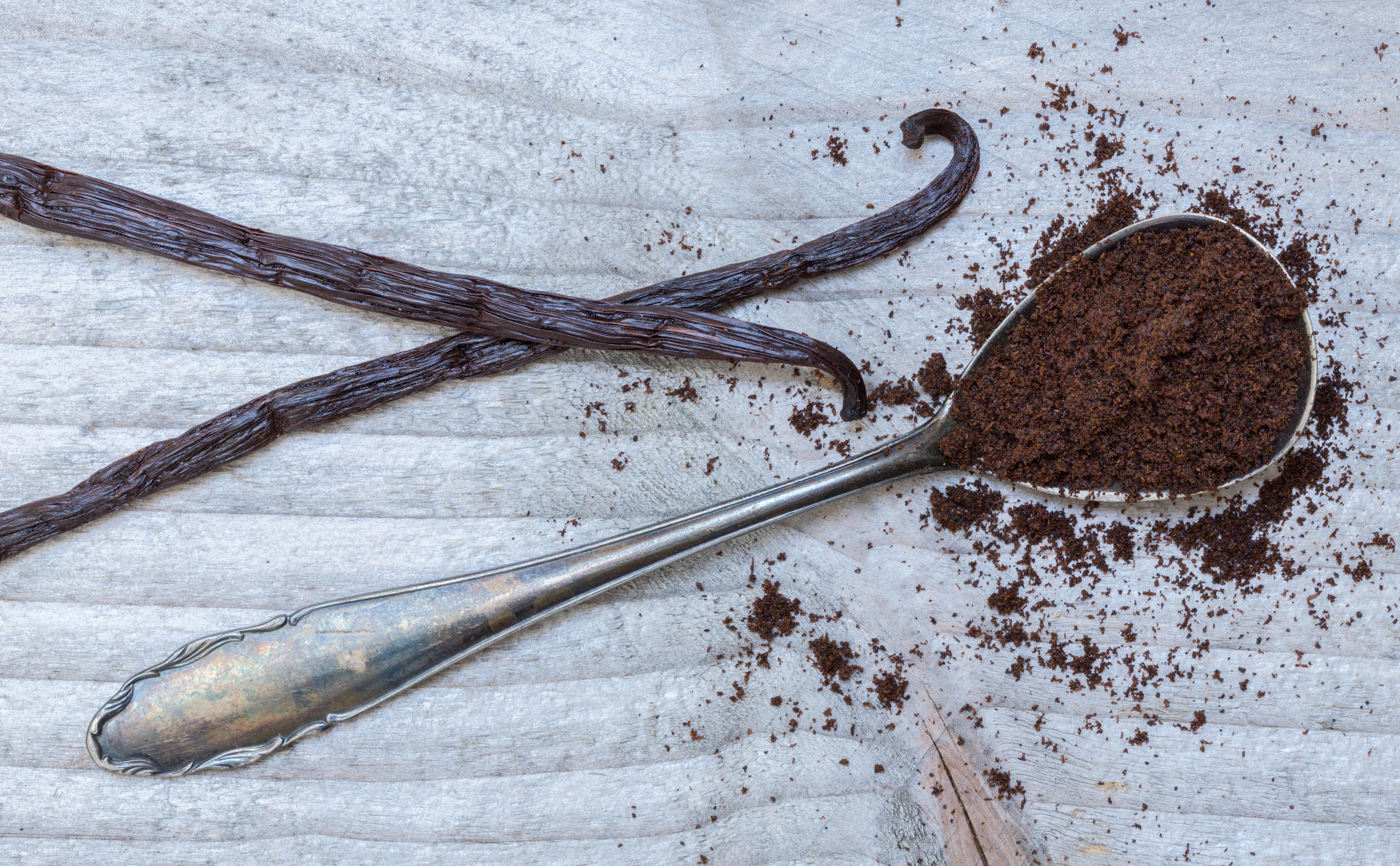 Vanilla bean, ground coffee, and a spoon with coffee grounds on a textured surface
