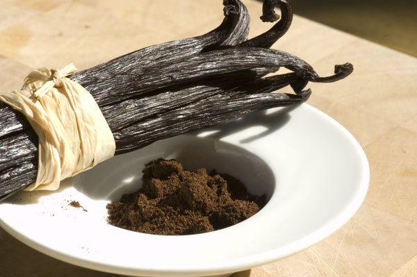 Vanilla beans and vanilla powder on a white plate with a wooden background